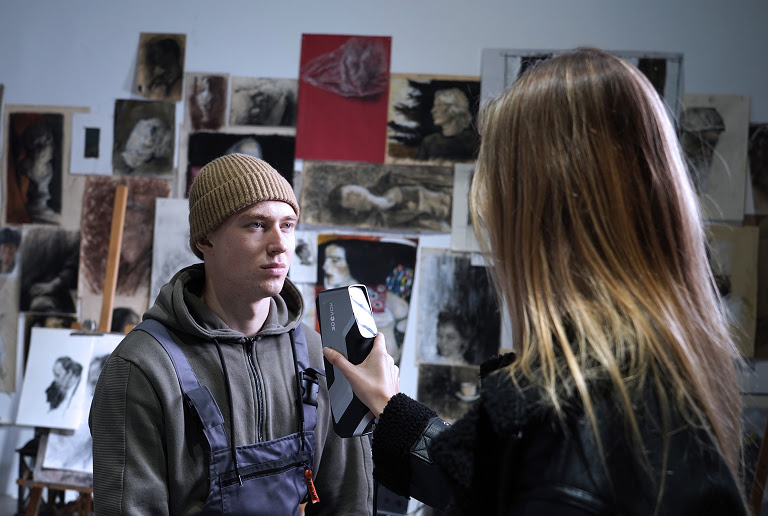 Woman 3D scanning a man in a beanie and hoodie.
