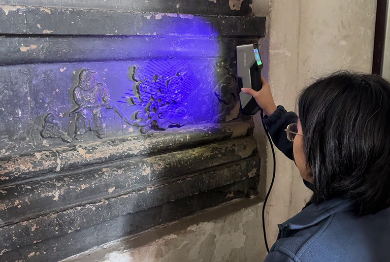 Woman  holding a 3DeVOK MT 3D scanner scanning ancient wall carvings 