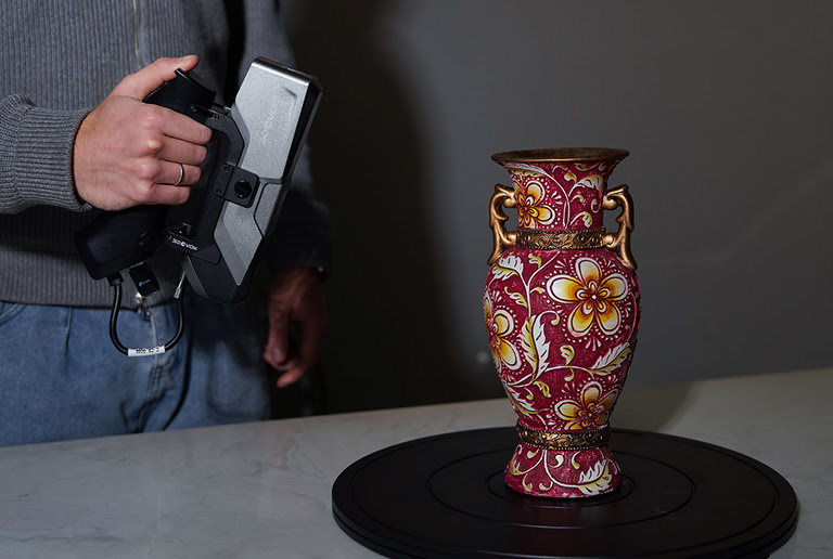 Hand holding the 3DeVOK MT Gen2 with the Airgo Wireless handle, 3D scanning a red vase with a flower pattern.
