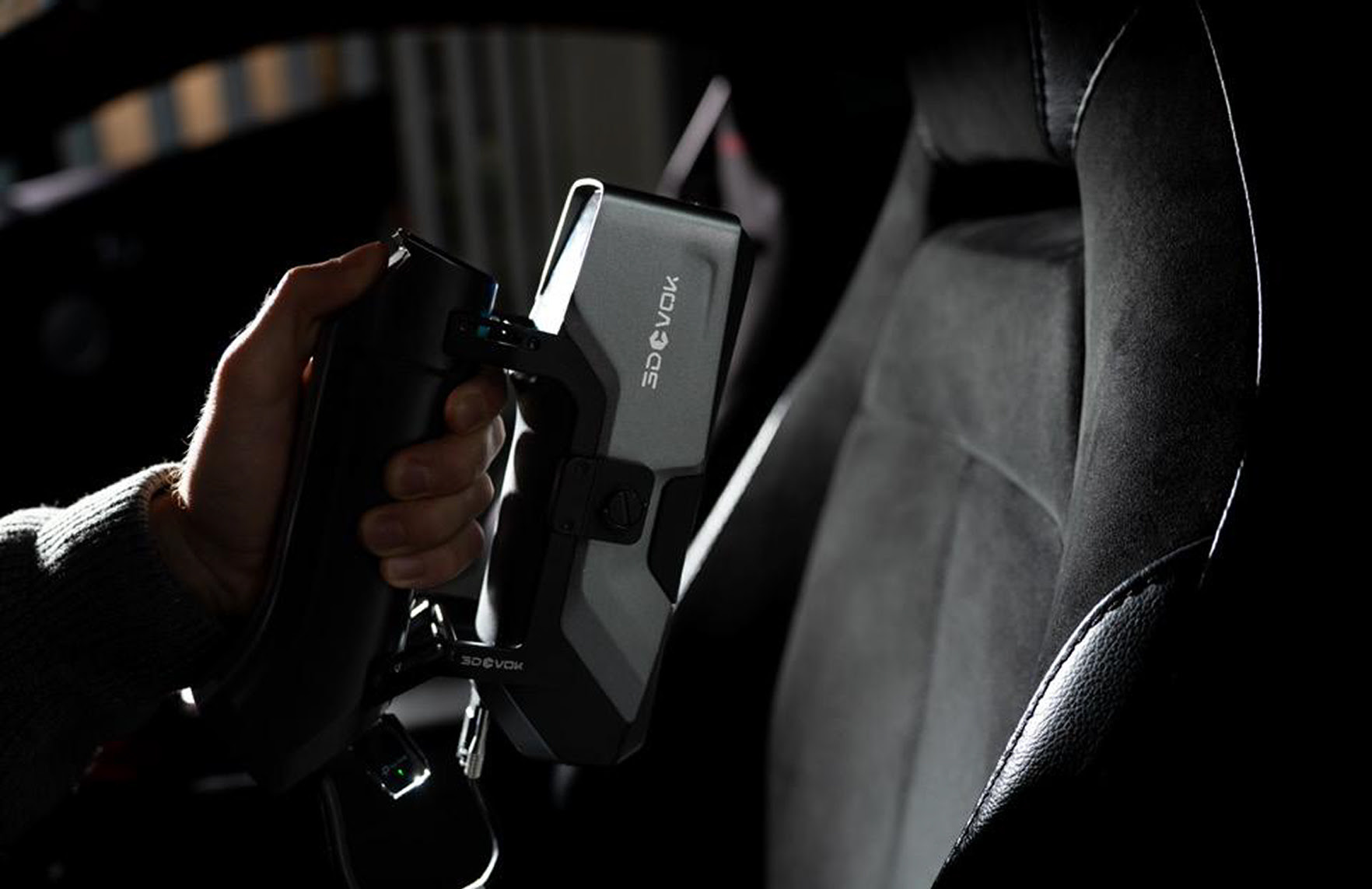 Hand holding the 3DeVOK MT Gen2 with the Airgo Wireless handle, 3D scanning a dark velvet car seat inside a car.