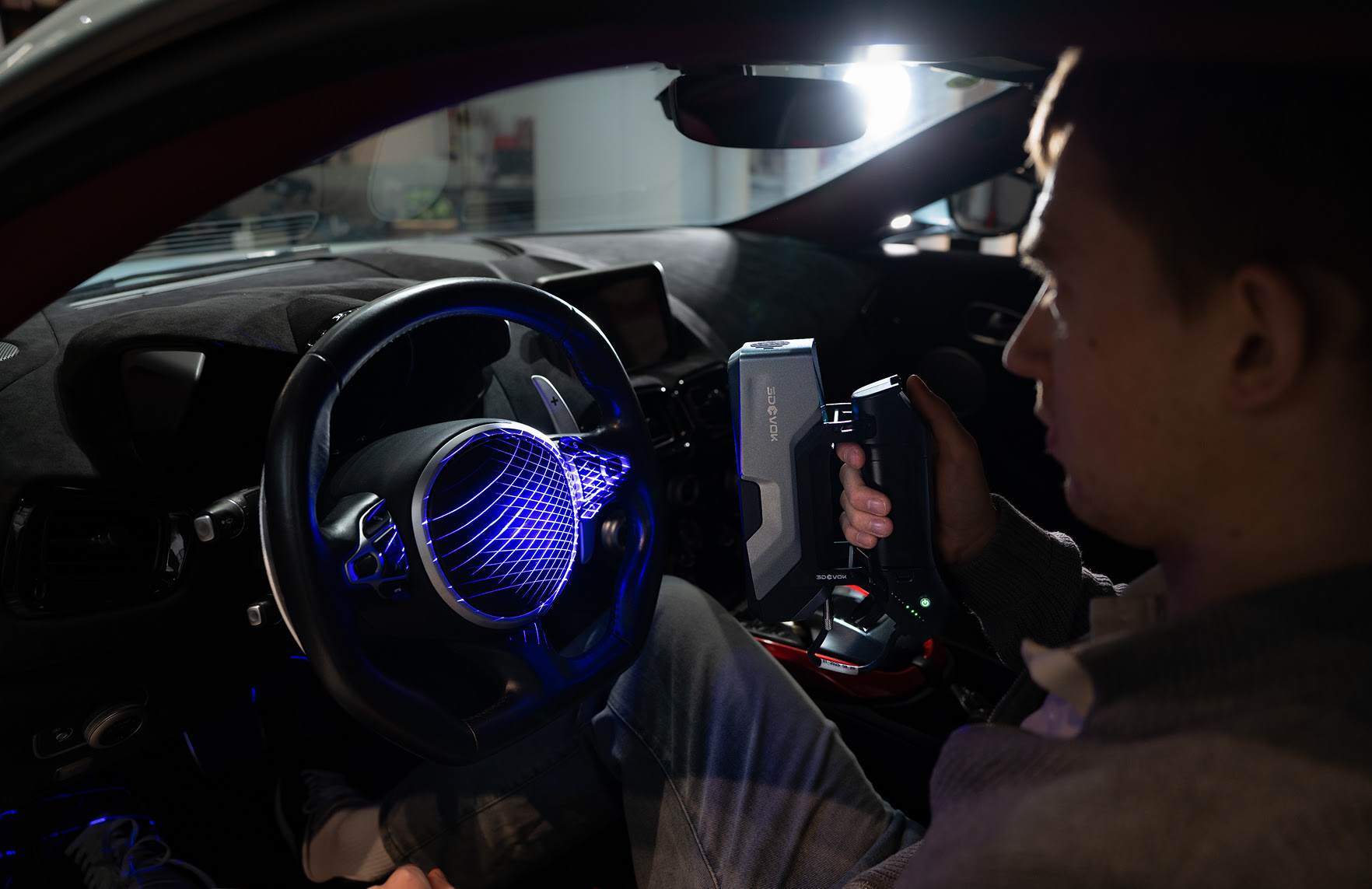 Person sitting inside a car holding the 3DeVOK MT Gen2 with the Airgo Wireless handle and 3D scanning the steering wheel.