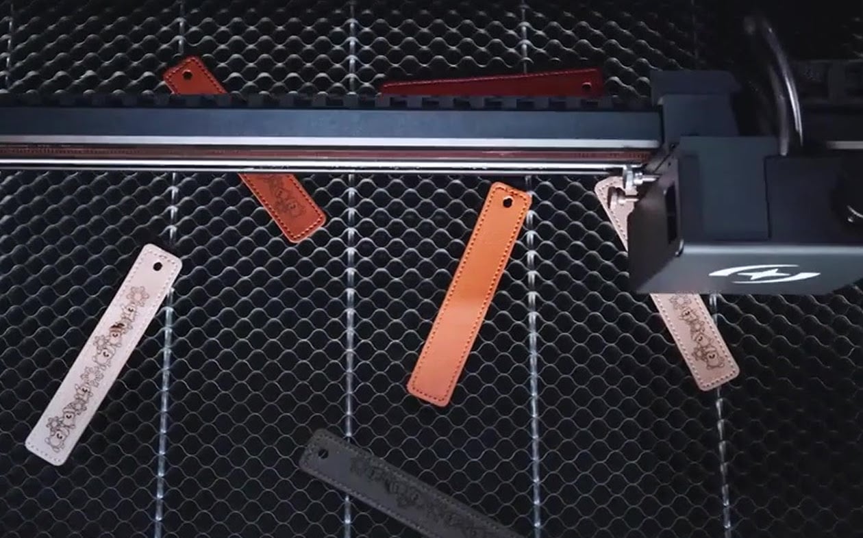 Several leather tags scattered on the honeycomb while the laser cutter is engraving a design.