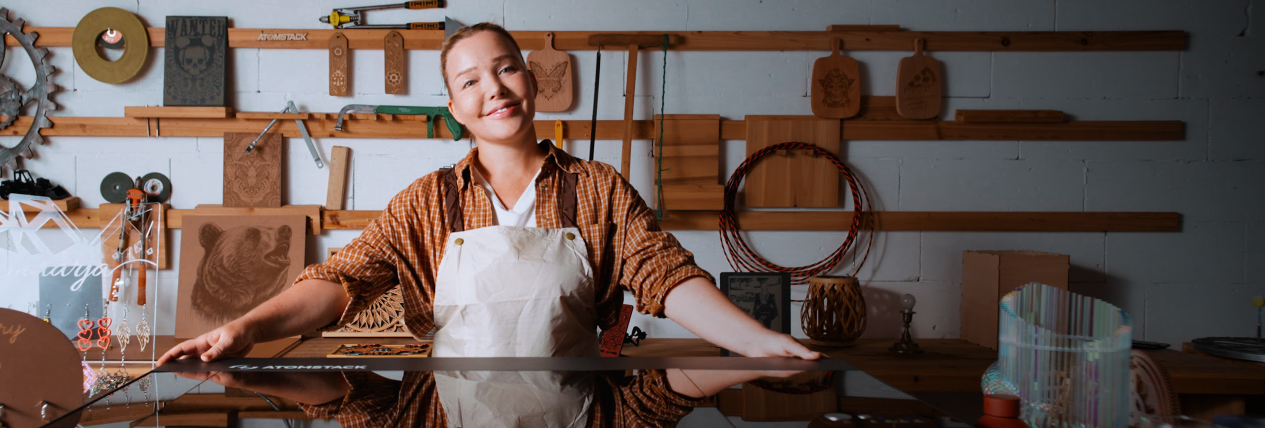 Smiling woman in a workshop standing behind an AtomStack Hurricane with her arms outstretched and holding onto the lid.