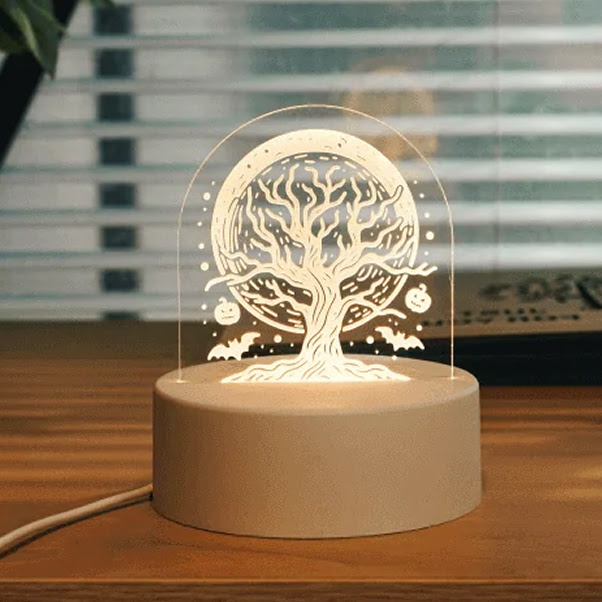 Piece of acrylic with a laser cut design of a tree and moon. The acrylic has been placed on a wooden base with a light so the engraved design gets illuminated.