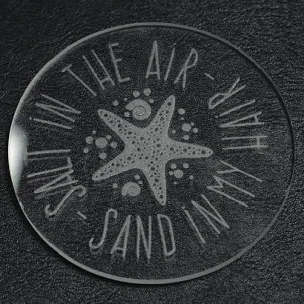 Glass disc with a laser engraved design of a starfish and the text: salt in the air, sand in my hair.