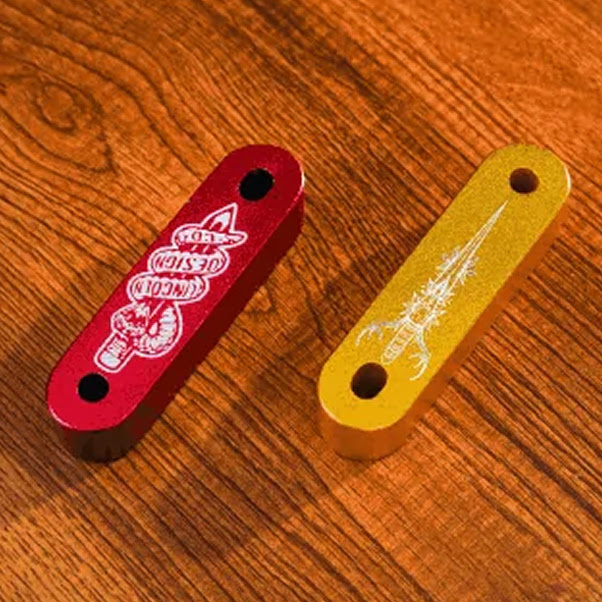 Two pieces of aluminium in red and yellow with a laser engraved design of a snake coiling around a pencil and a dagger with antlers.