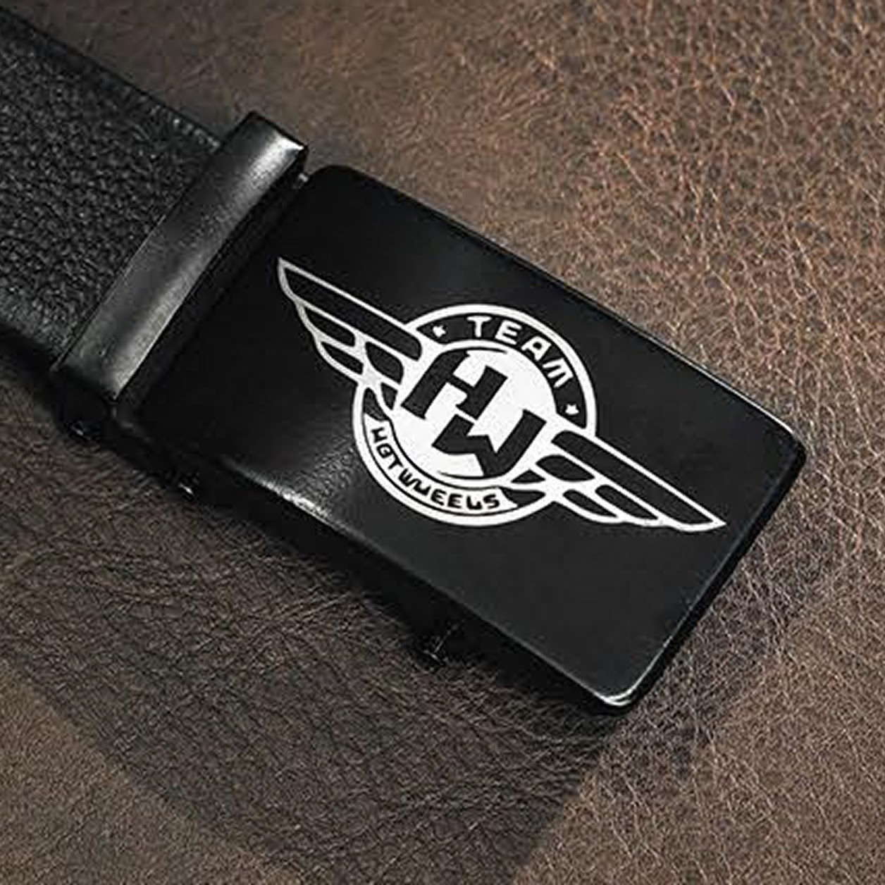 Belt buckle in black metal with a laser engraved design of a logo of a circle with wings and the text Team Hotwheels.