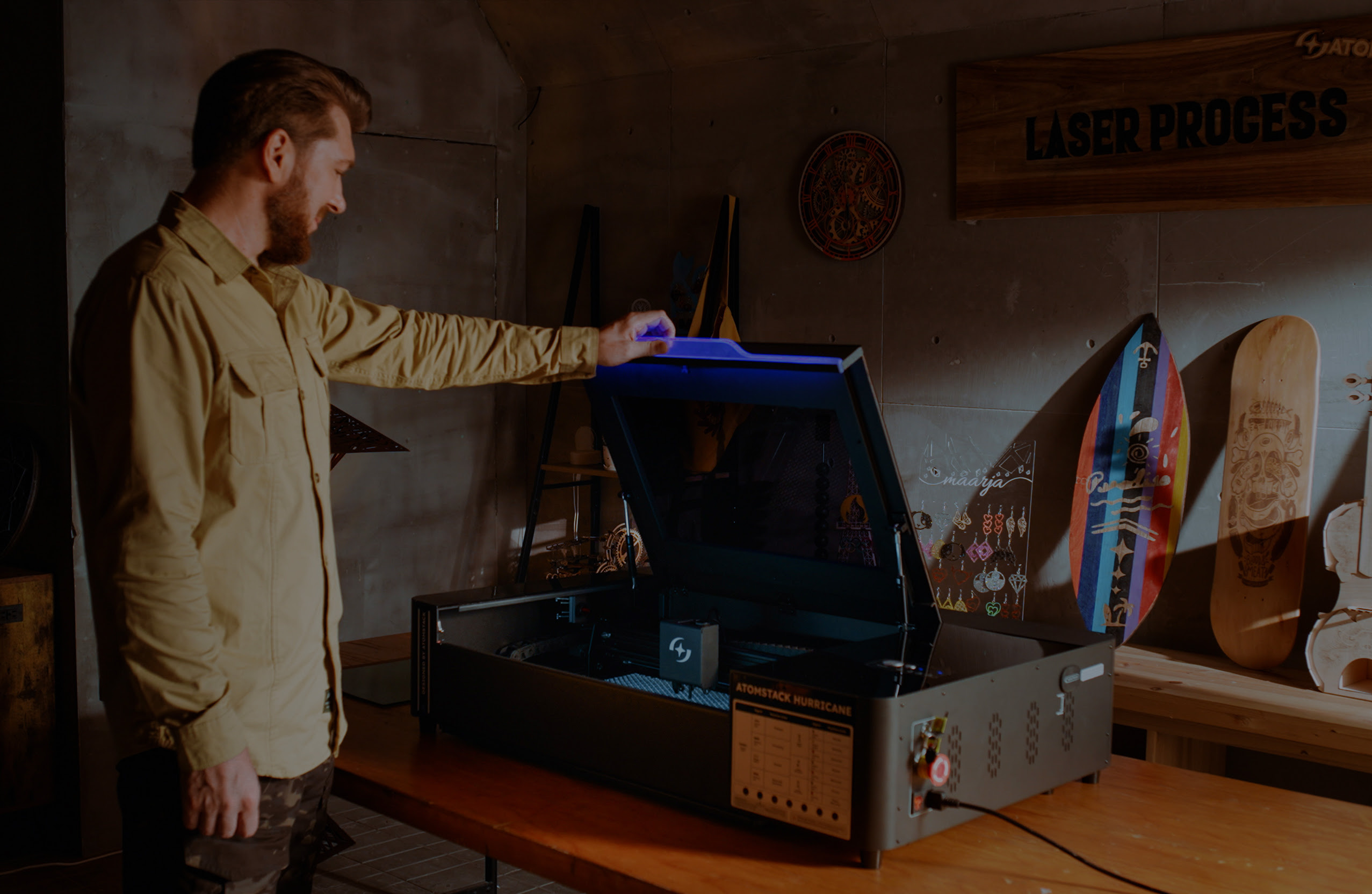 A man in a workshop holding the lid of the AtomStack Hurricane open. The blue led light of the lid is on.