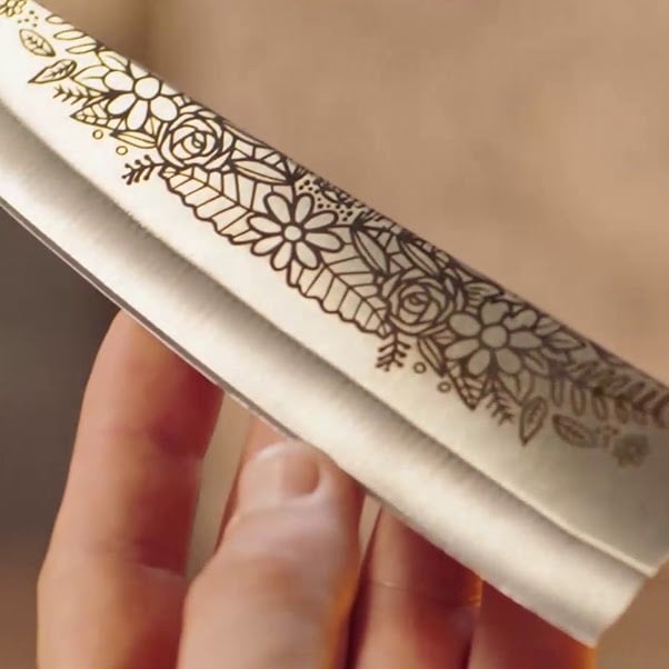 Hand holding the blade of a knife with a laser engraved design of flowers