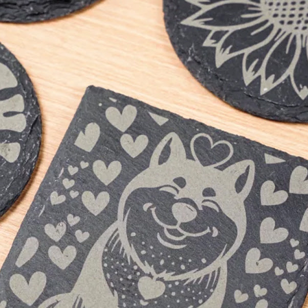 Piece of square slate with an engraved design of a cute dog surrounded by hearts.