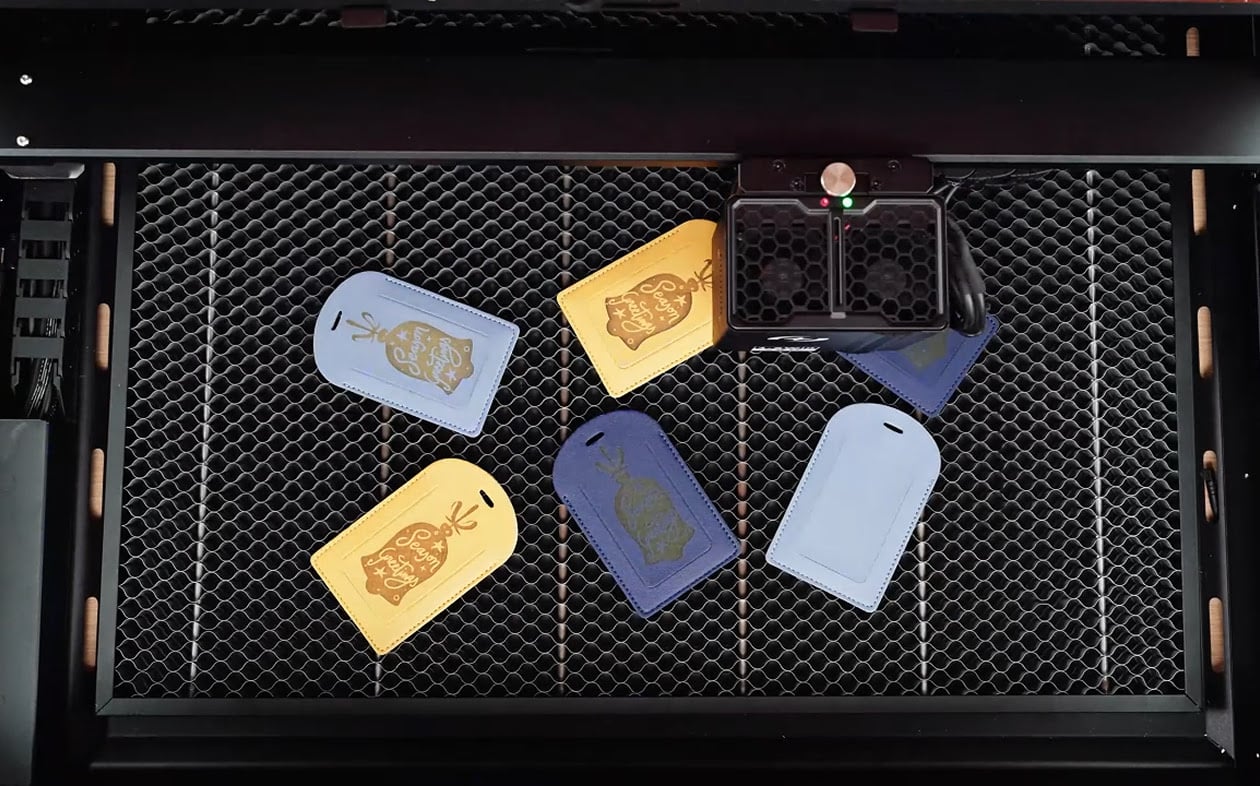 Several leather tags scattered on the honeycomb while the laser cutter is engraving a design.