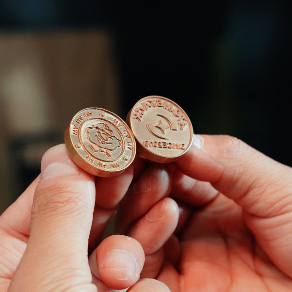 Two hands holding two milled brass stamps.