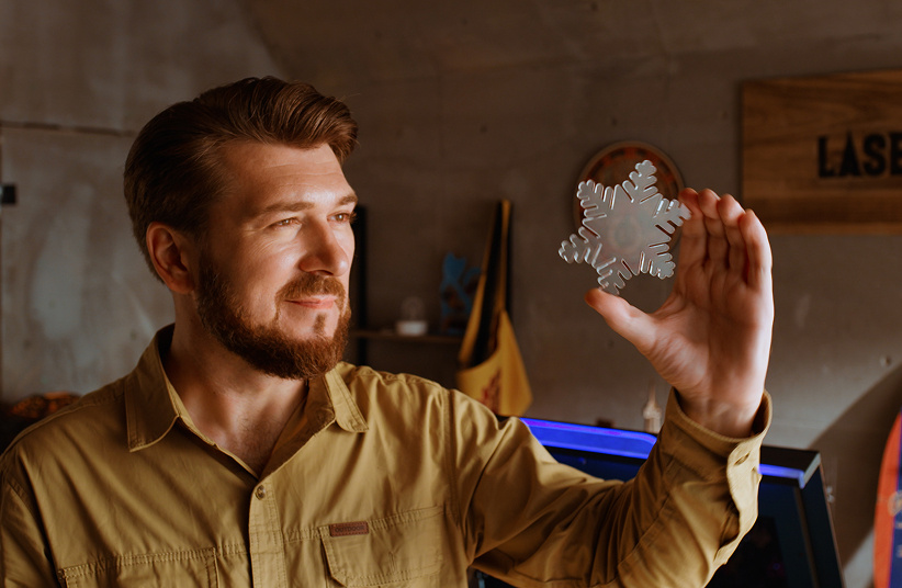 Man holding a lasercut acrylic snowflake in his left hand and admiring it.