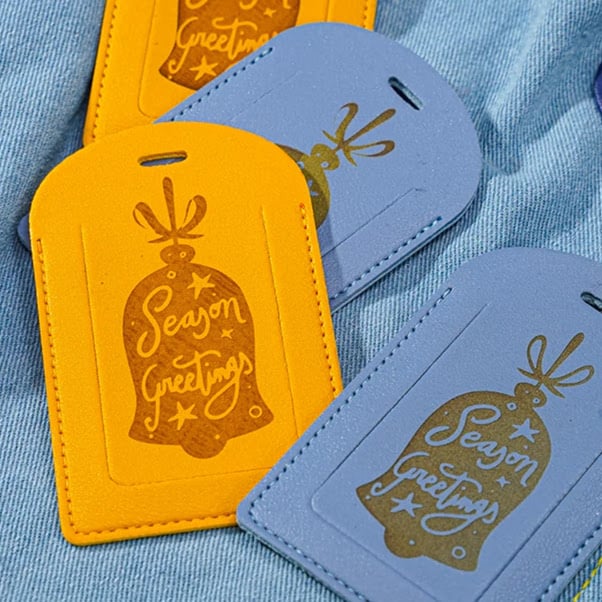 Leather tags in blue and yellow with a laser engraved design of a bell and the text Season greetings
