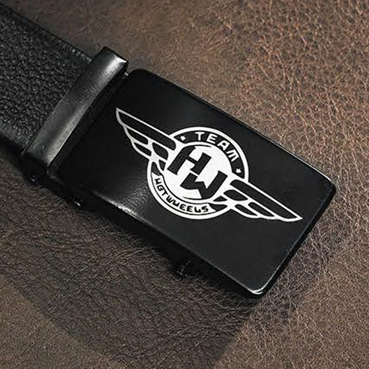 Belt buckle in black metal with a laser engraved design of a logo of a circle with wings and the text Team Hotwheels.