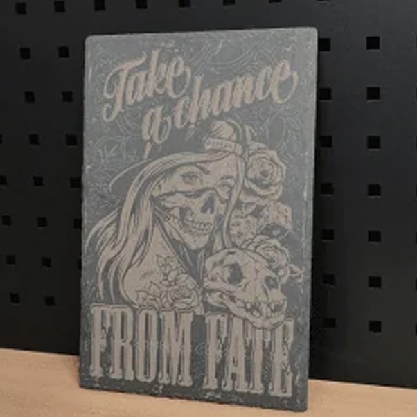 Piece of rectangular slate standing upright. It has a laser engraved design of a female skull with long hair and a cap. It has the text: take a chance from fate.
