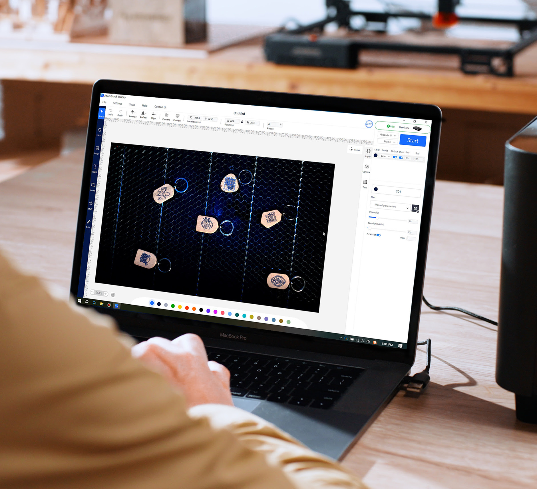 Looking over the shoulder of a man working on a laptop with AtomStack Studio open. The camera preview is showing 6 items on the honeycomb.