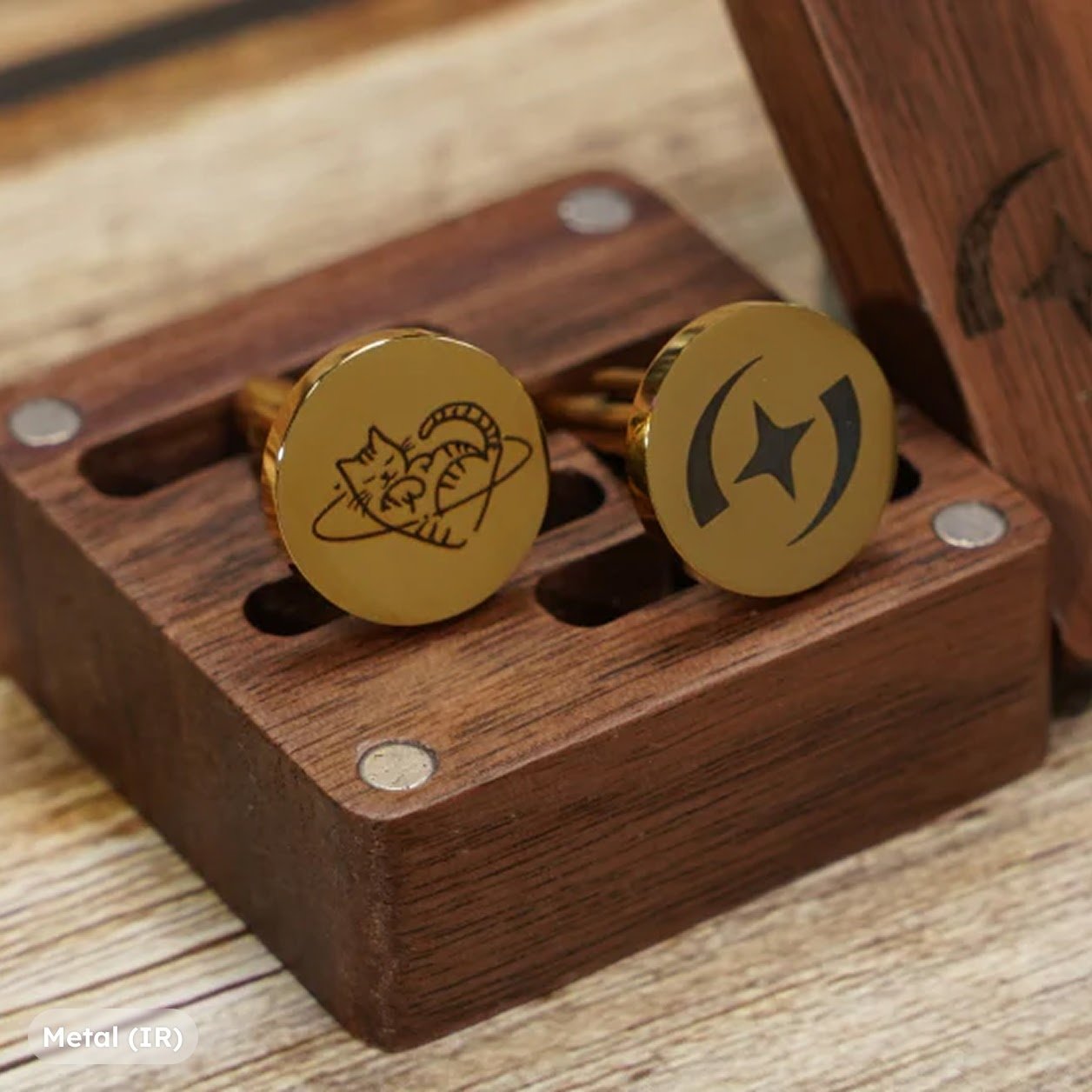 Two metal cufflinks, one with an engraved AtomStack logo and the other a sleeping cat illustration.