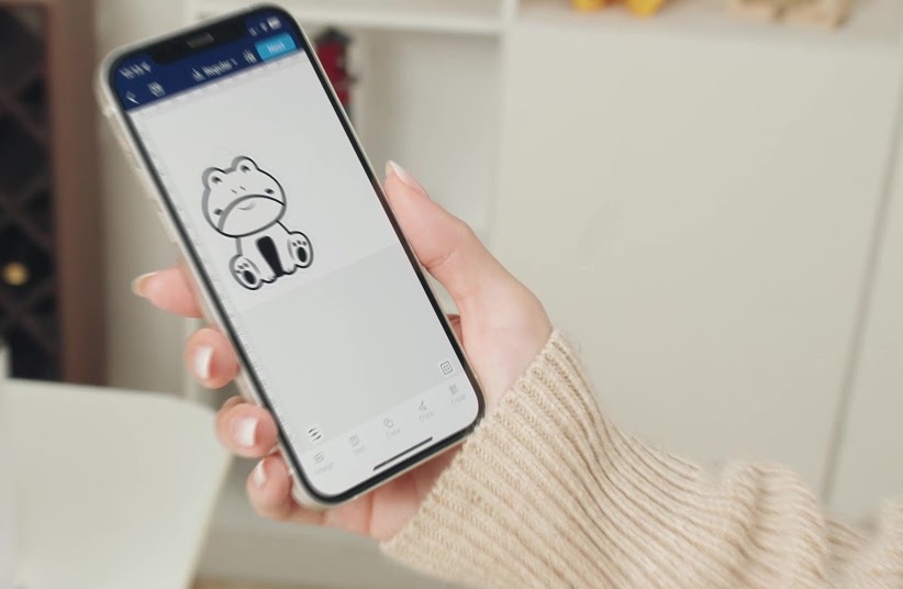 Hand holding a smartphone with AtomStack Studio opened and a design of a cat on the canvas.