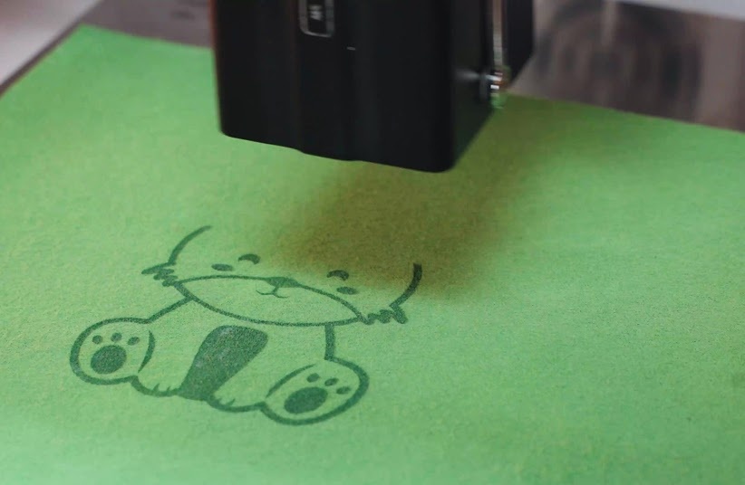 Close-up of a cat illustration being engraved on green felt.
