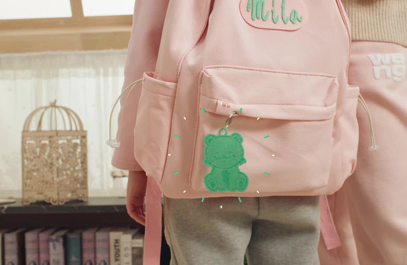 Green felt engraved keychain of a cat illustration dangling on a backpack.