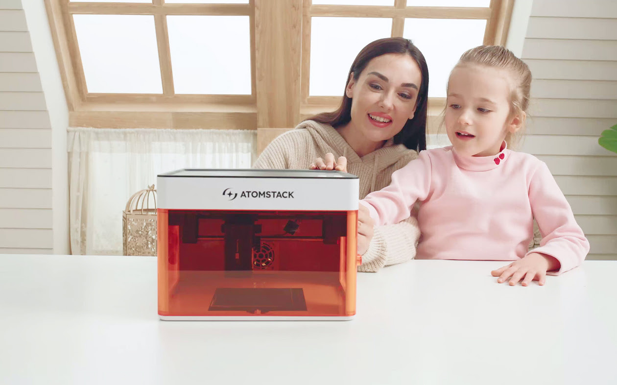 Woman and young child sitting at a table. They are touching the AtomStack P1 that stands in front of them.