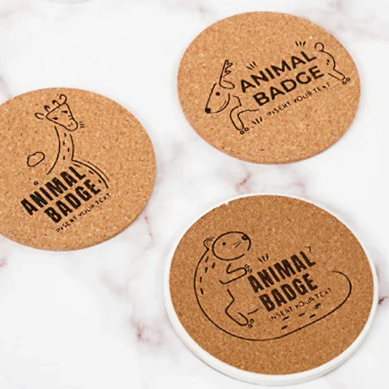 Three cork coasters with a lasercut design of a giraffe, deer or beaver and the text Animal Badge.