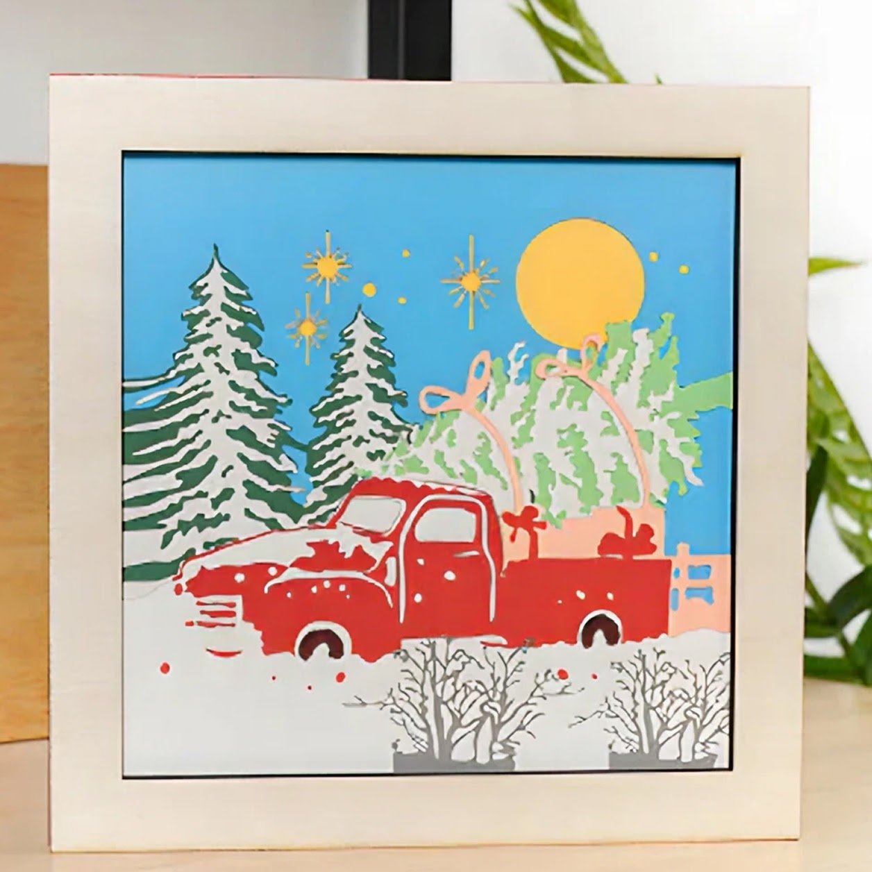 Papercut framed scene of a red truck in a snowy landscape with a christmas tree in the trunk.