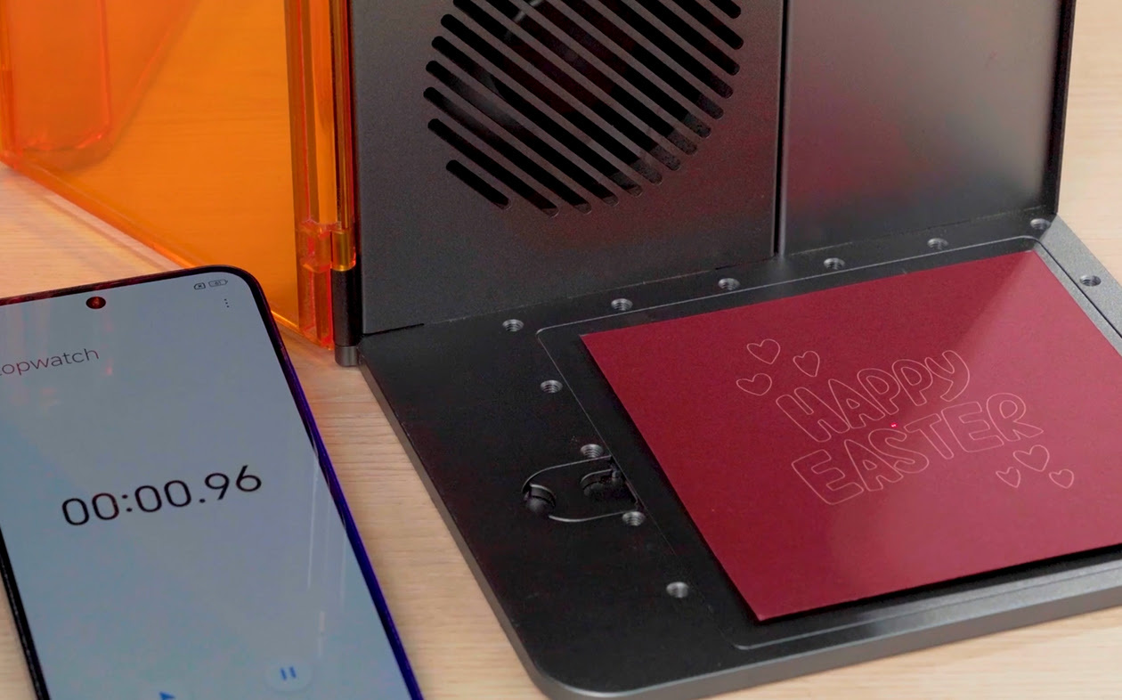 Close-up of the AtomStack Atelier having engraved craft paper. A mobile phone showes a timer with 00:00.96