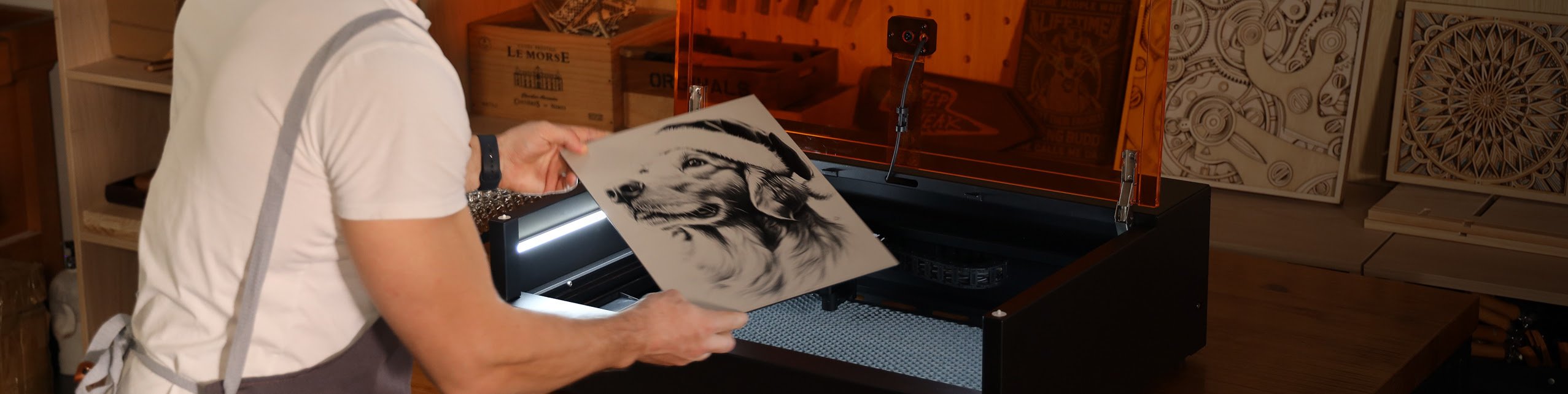 Man holding an engraved piece of wood in front of an open AtomStack Kraft 40 W.