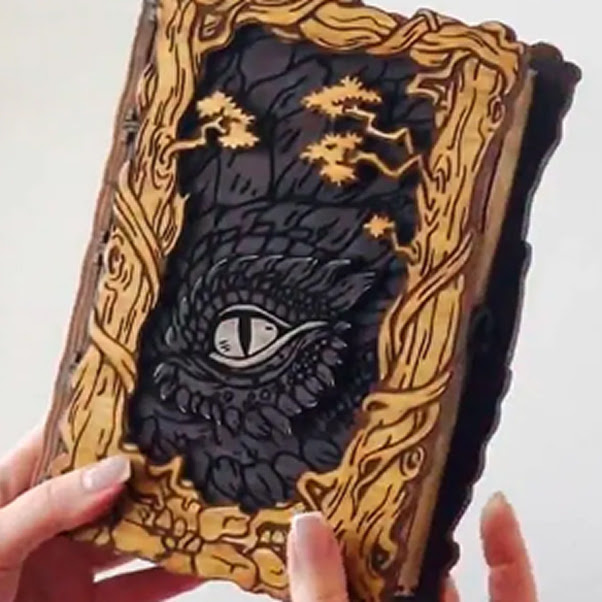 Engraved wooden cover of a book depicting a forest and vines, and the eye of a dragon peeking through.