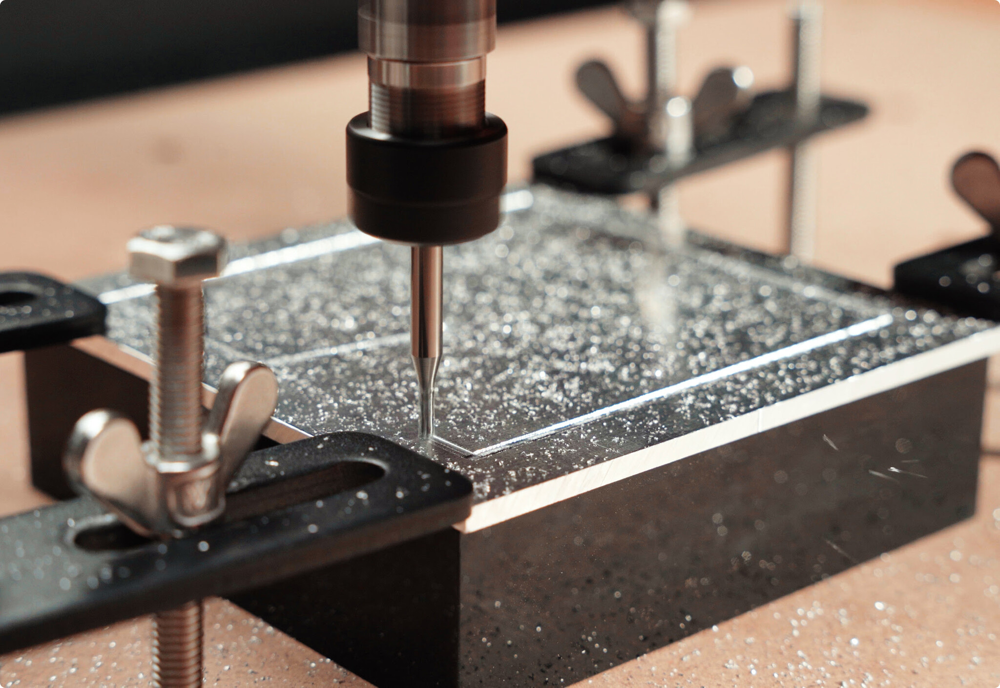 Close-up of a CNC milling machine precision-cutting a metallic plate secured on a workbench with hold-down clamps.