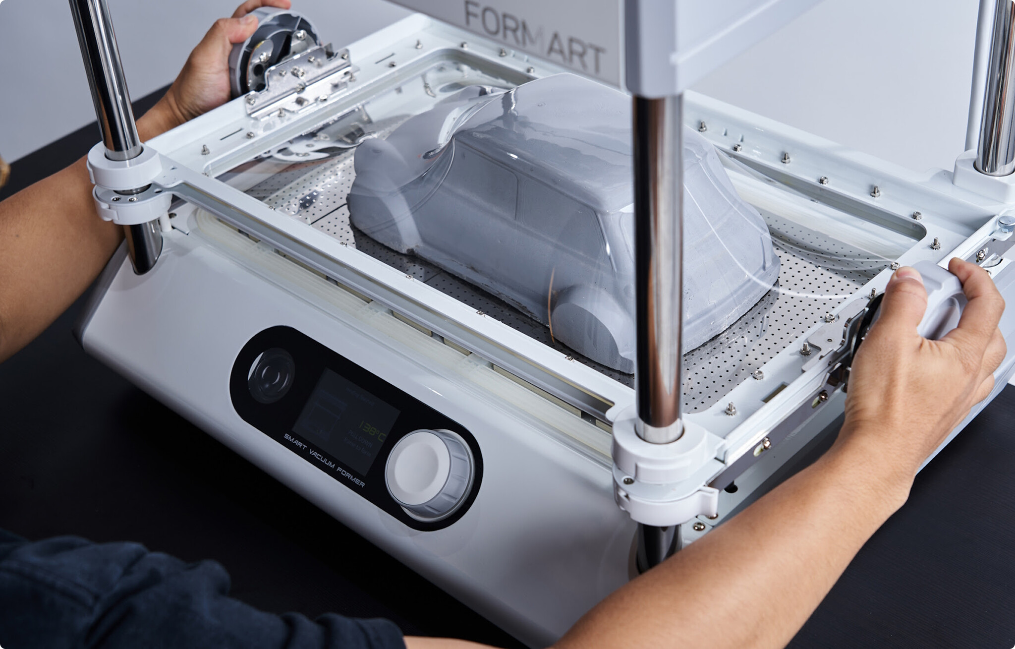 A person using a MY YARD FORMART vacuum former machine to mold clear plastic over a gray miniature car.