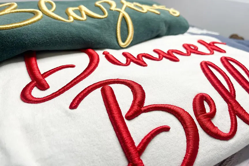 Close-up of 3D puff embroidered cursive lettering on fleece sweatshirts produced by a BAi commercial multi-needle embroidery machine