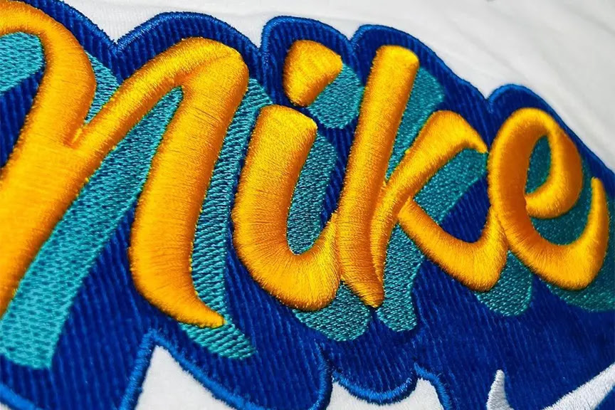 Extreme close-up of vibrant multi-color satin stitch embroidery with raised yellow detail stitched on a commercial BAi machine